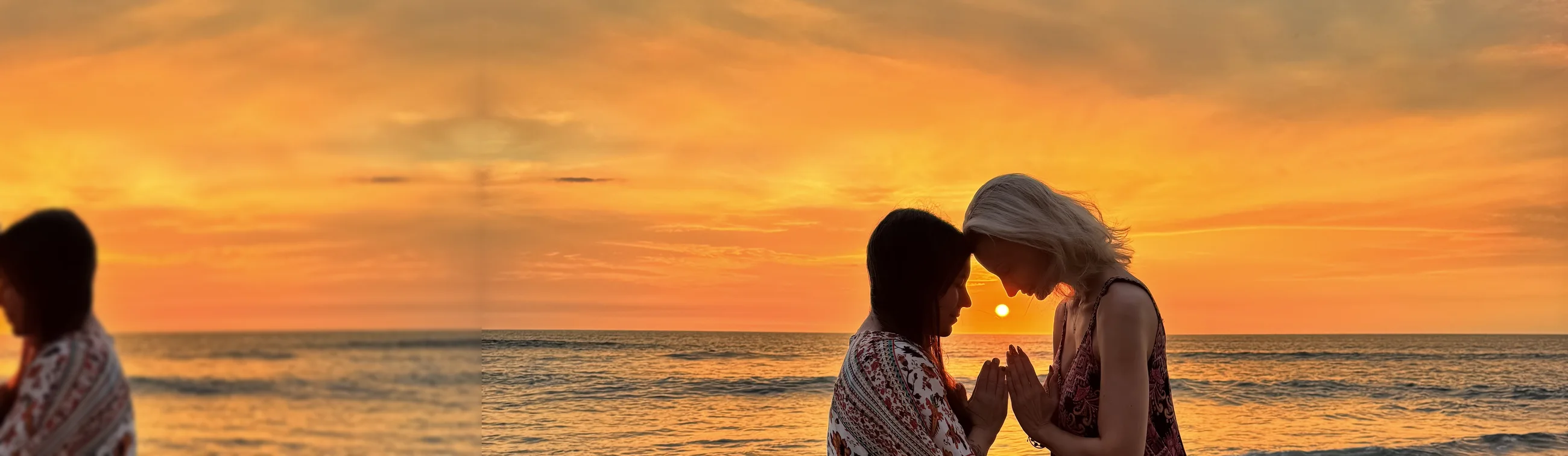 Two women in sunset ceremony, foreheads touching, the sun between their hands